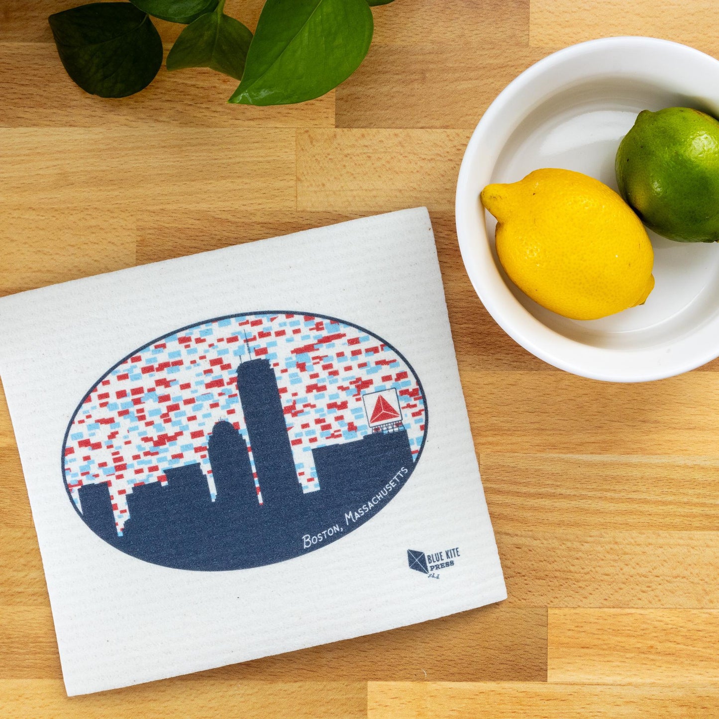 Boston skyline Swedish dishcloth featuring Citgo sign design on wooden surface with bowl of citrus fruits and green leaves, showcasing eco-friendly kitchen accessory and sustainable lifestyle