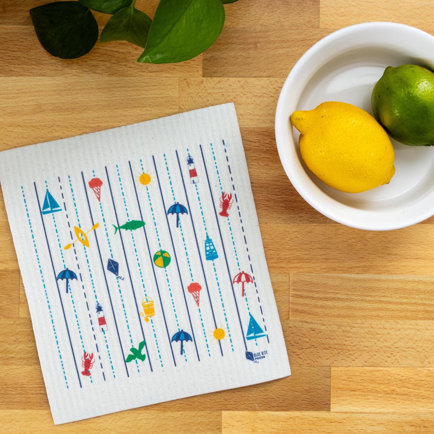 Sustainable Swedish dishcloth with colorful New England coastal icons on wooden surface, next to bowl with lemon and lime, showcasing eco-friendly alternative to paper towels