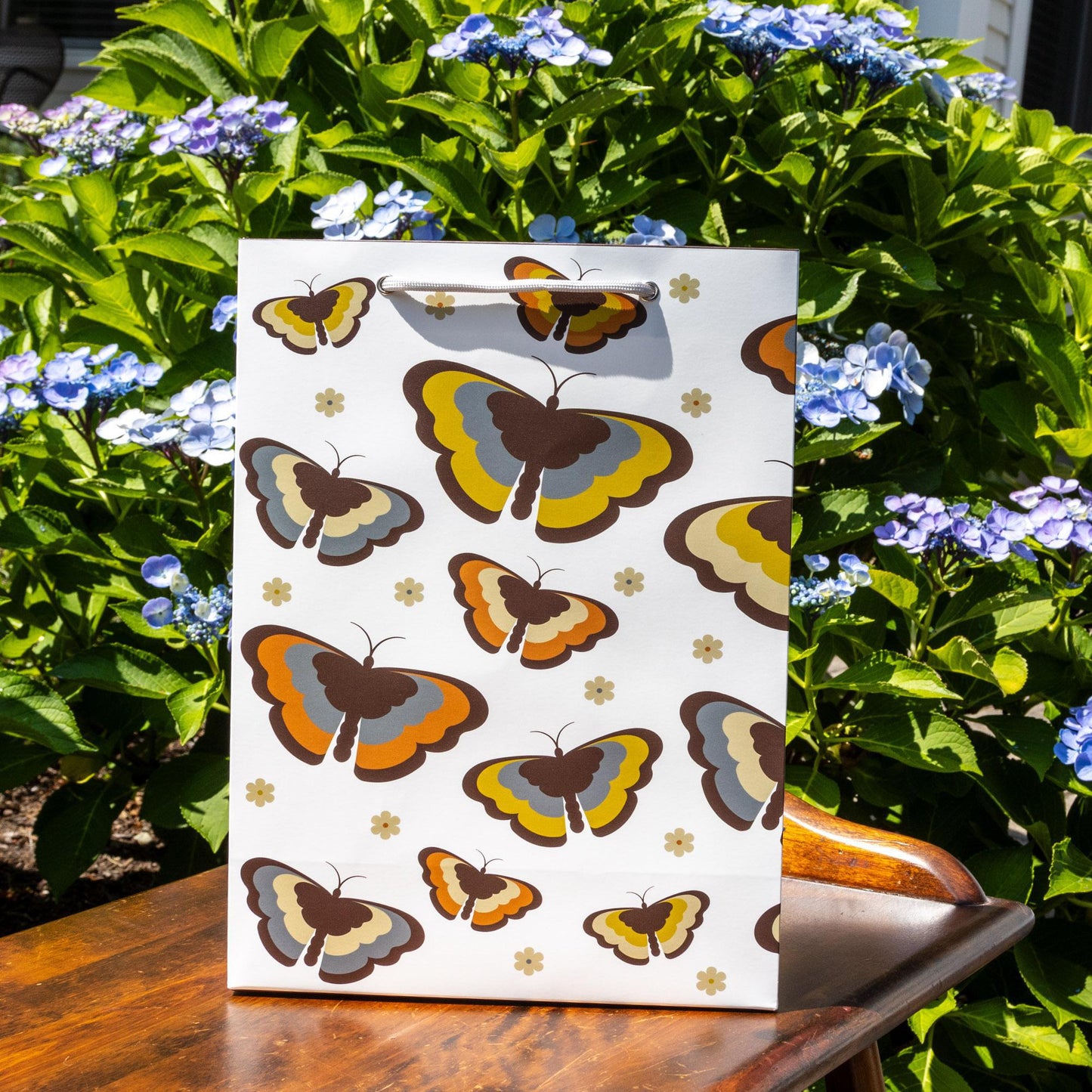 Retro-inspired gift bag featuring colorful butterfly pattern in 70s style colors, surrounded by blooming blue hydrangea flowers, showcasing the product's vintage aesthetic and matte paper finish