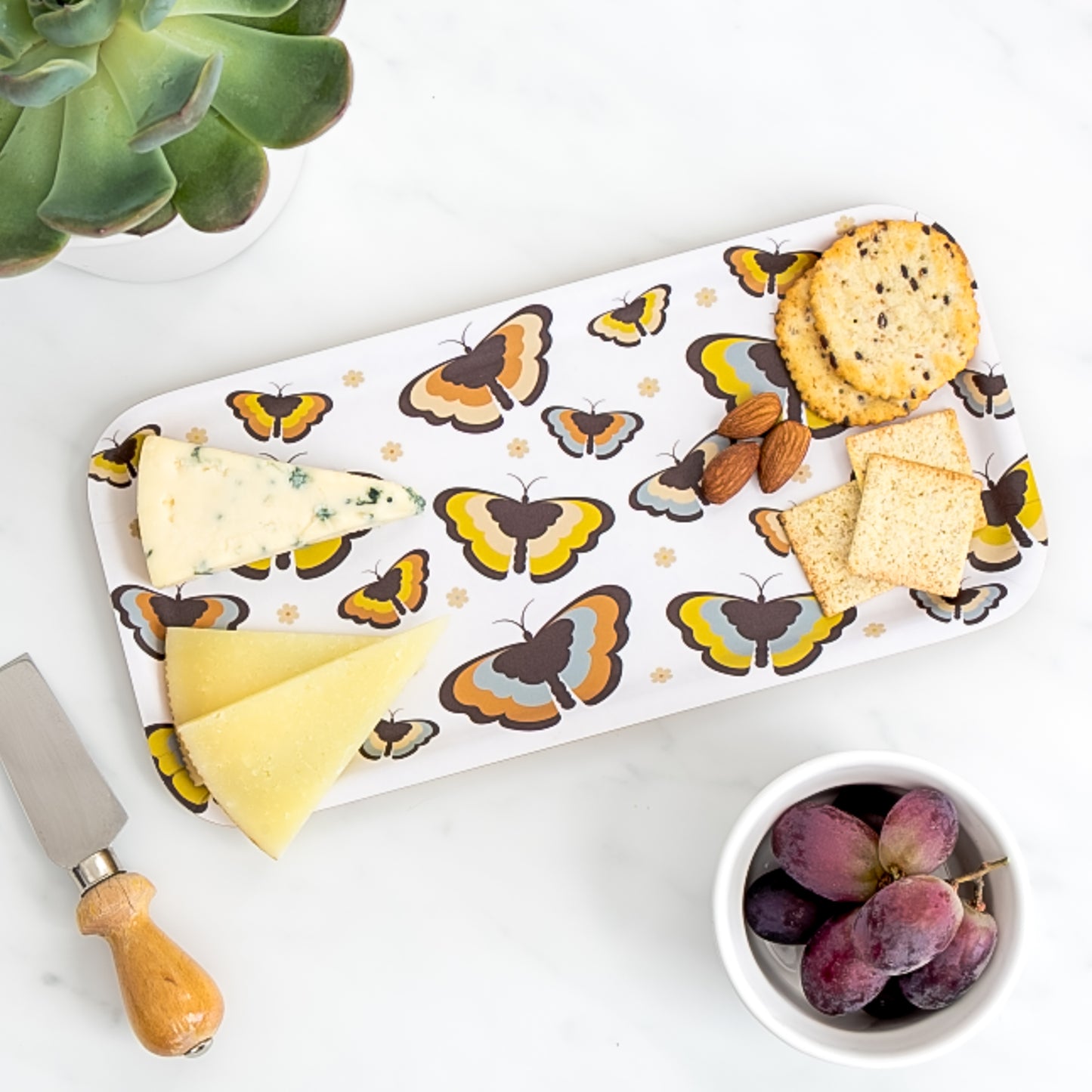 Cheese board of assorted cheese and crackers on birch tray with 70s boho butterfly pattern