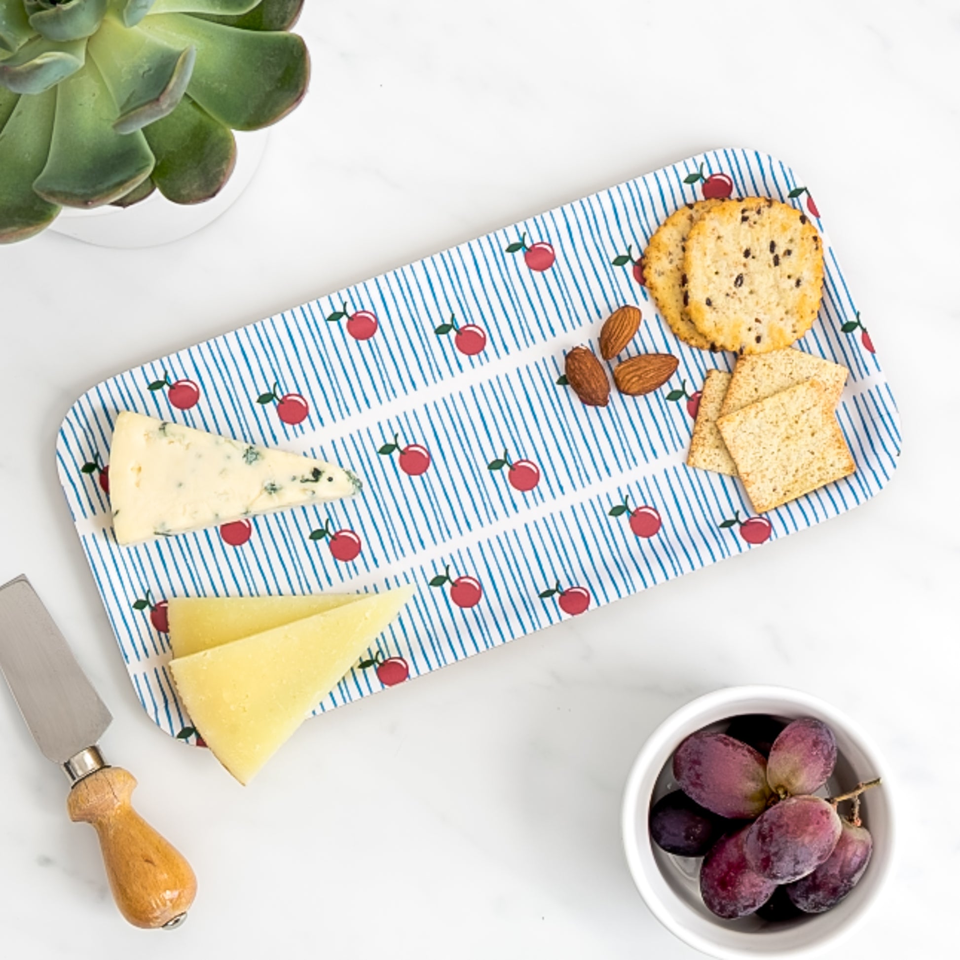 Cheese board of assorted cheese and crackers on birch tray with vintage cherry pattern