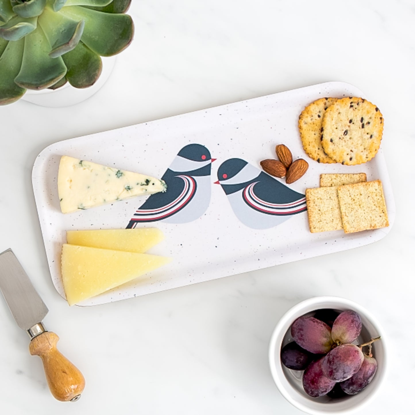 Cheese board of assorted cheese and crackers on birch tray with modern chickadee pattern