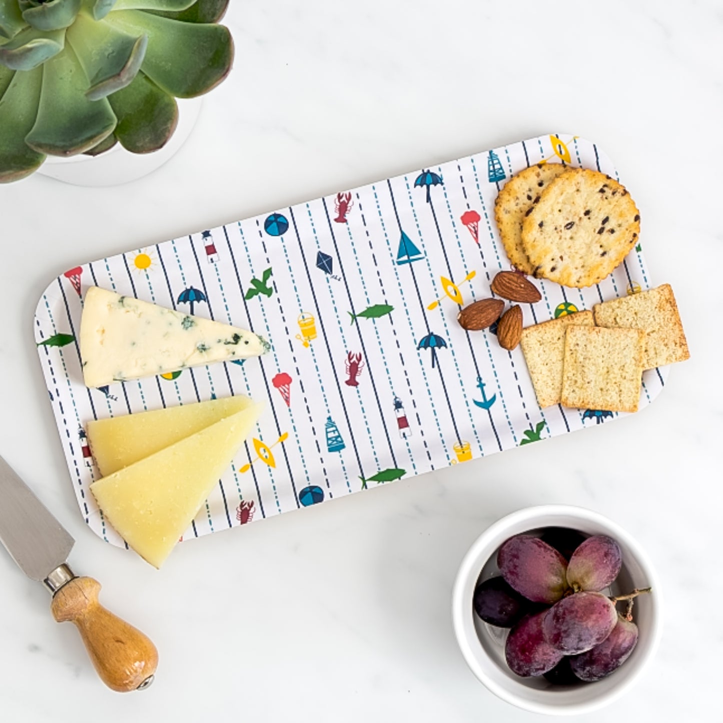 Cheese board of assorted cheese and crackers on birch tray with seaside pattern