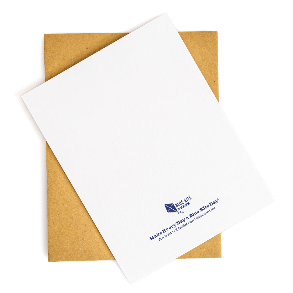 Blank white greeting card with blue text on back reading "Make Every Day a Blue Kite Day" with kraft envelope background