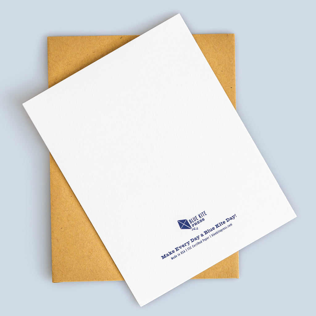White greeting card with Blue Kite Day logo and kraft envelope on light blue background