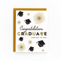 Graduation card with black caps, gold starbursts, and congratulations message with kraft envelope background