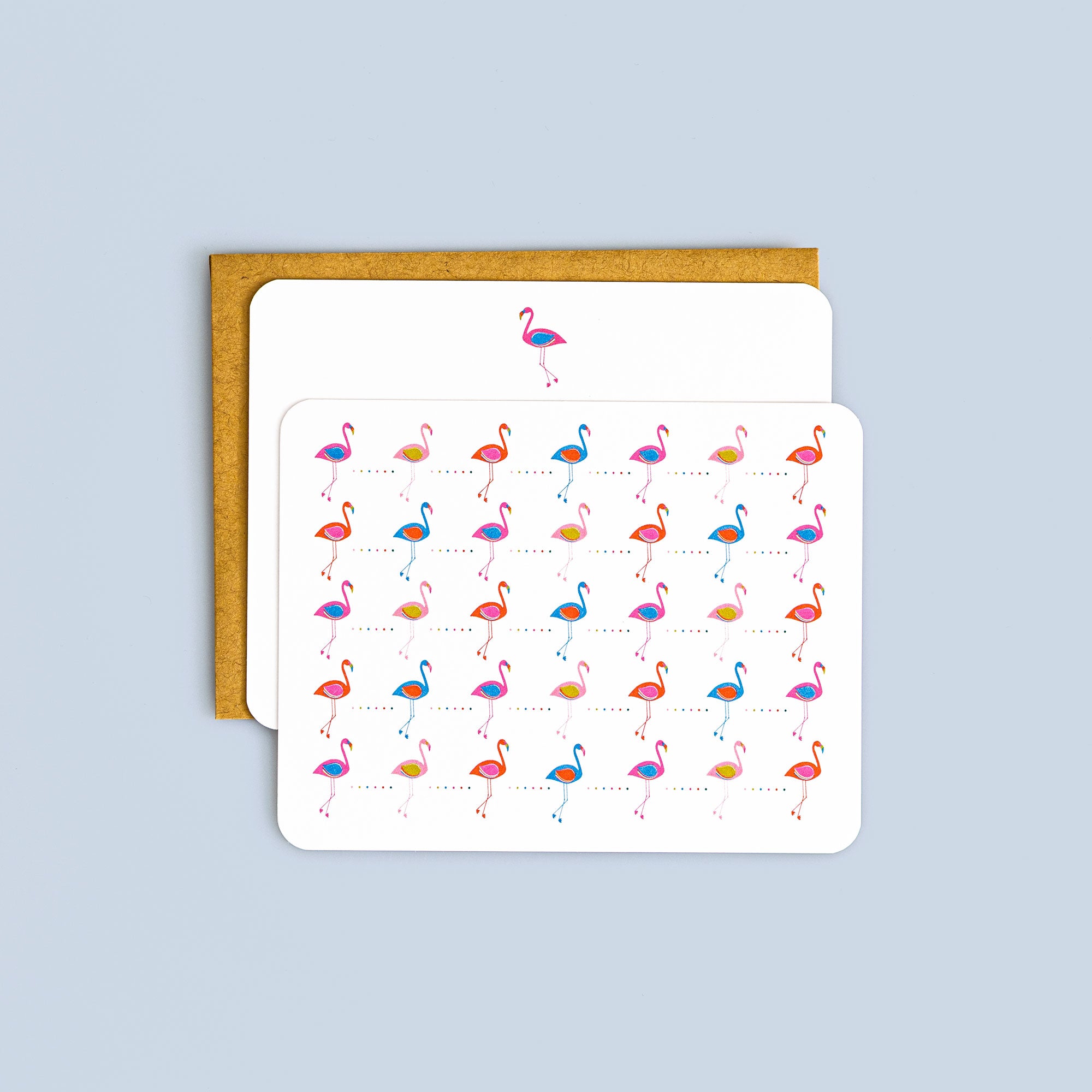 Box set of flat cards with colorful flamingo pattern and coordinating kraft envelopes on pale blue background