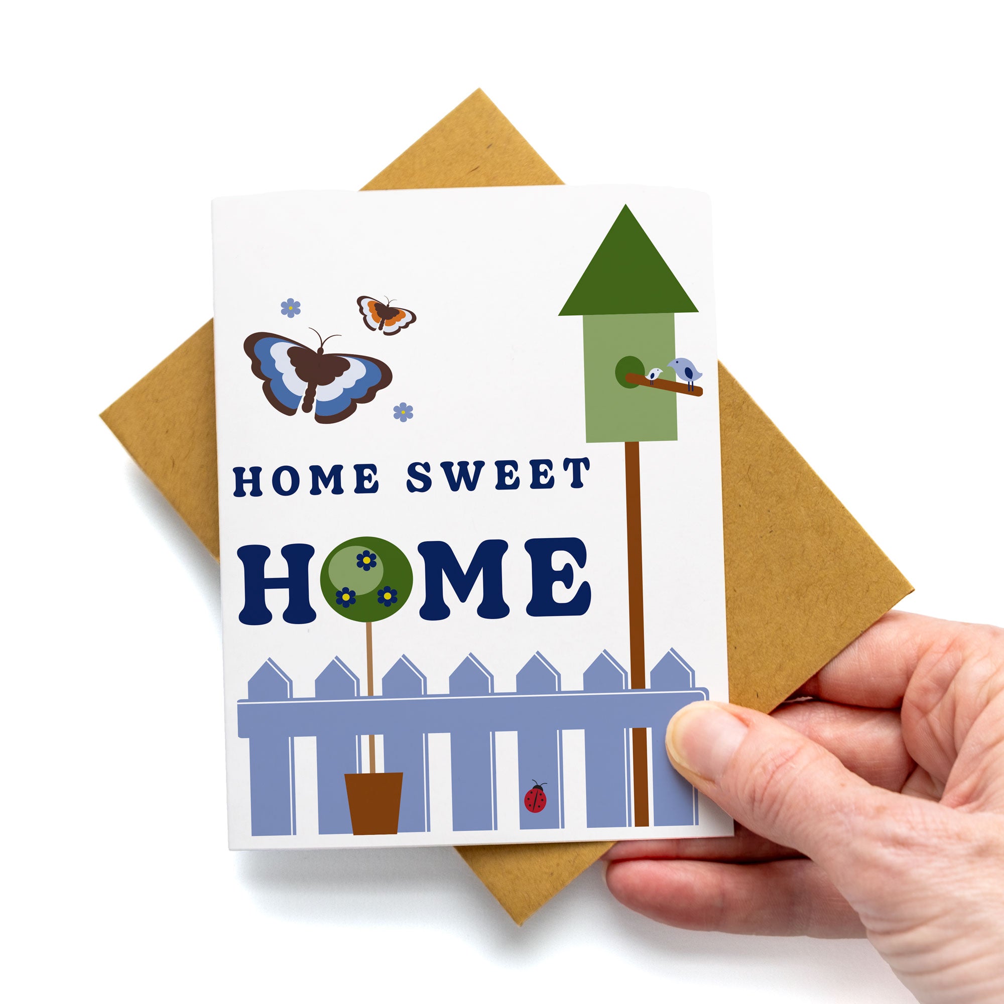 Home Sweet Home Card featuring butterflies, birdhouse, white picket fence, and garden scene, blank inside with kraft envelope.