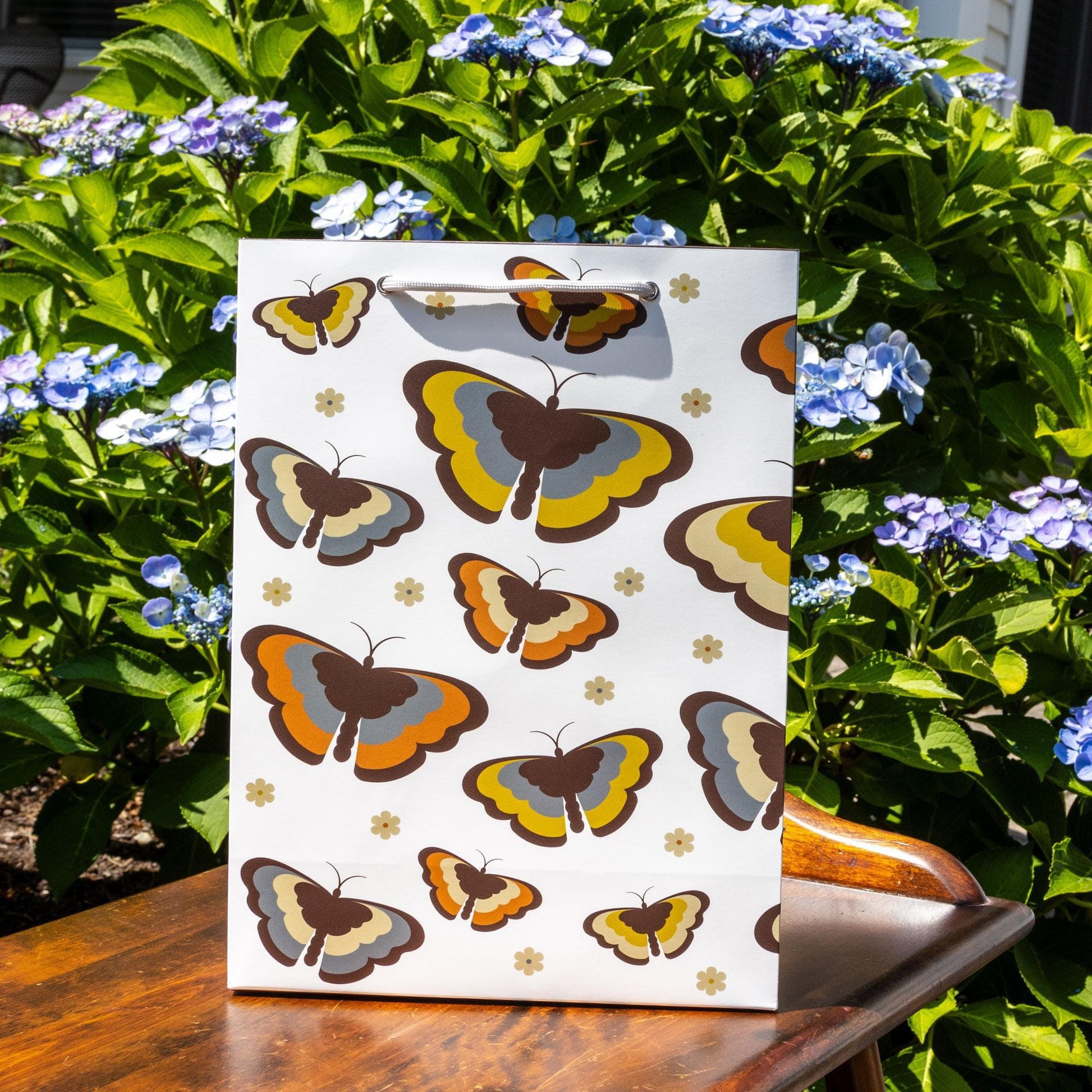 Retro-inspired gift bag featuring colorful butterfly pattern in 70s style colors, surrounded by blooming blue hydrangea flowers, showcasing the product&#39;s vintage aesthetic and matte paper finish