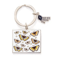Retro 70s style butterfly enamel keychain with yellow and brown butterfly designs on white background, silver ring, and Blue Kite Press charm