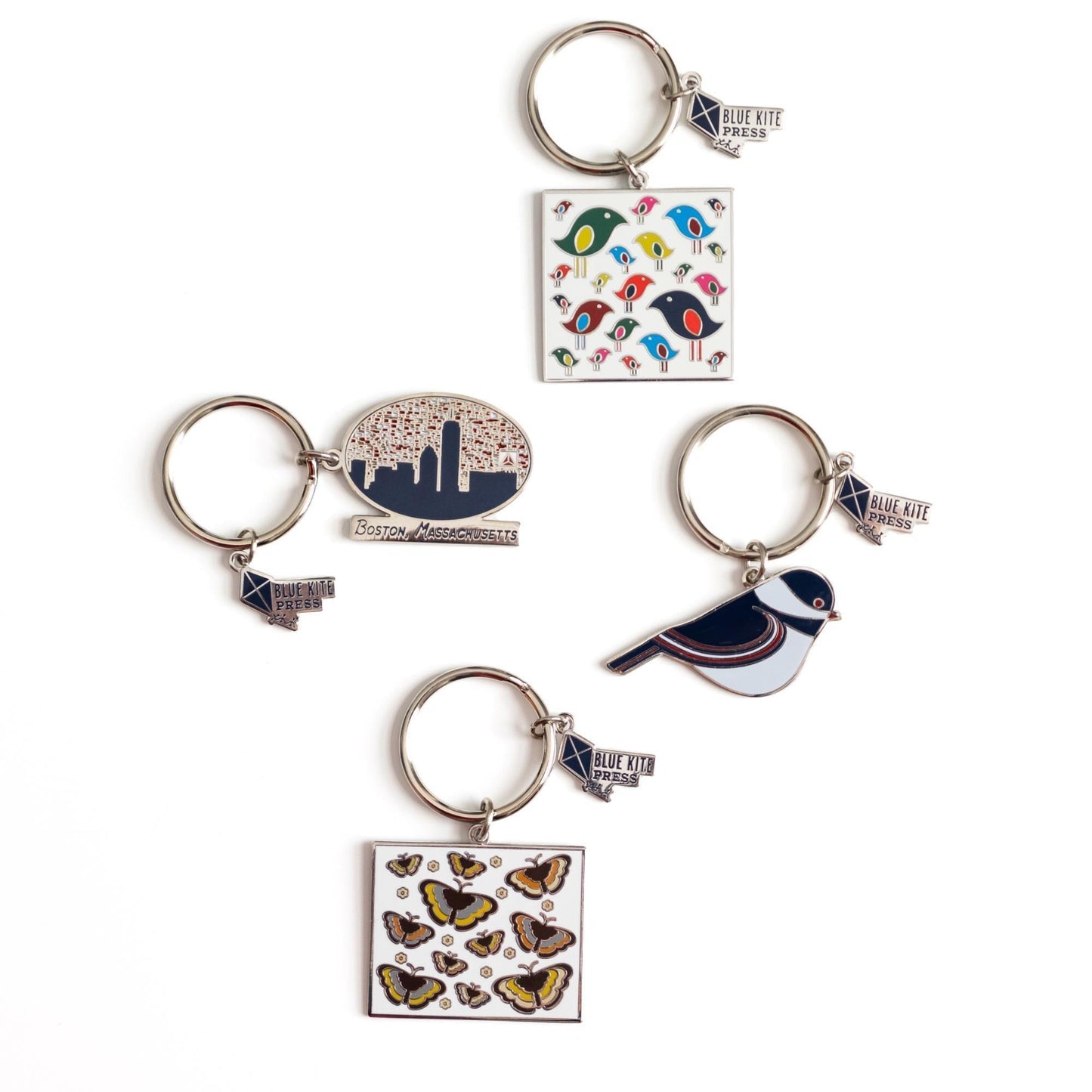 Assortment of enamel keychains featuring Boston skyline, colorful birds, butterflies, and a chickadee design, showcasing diverse and charming city-themed accessories