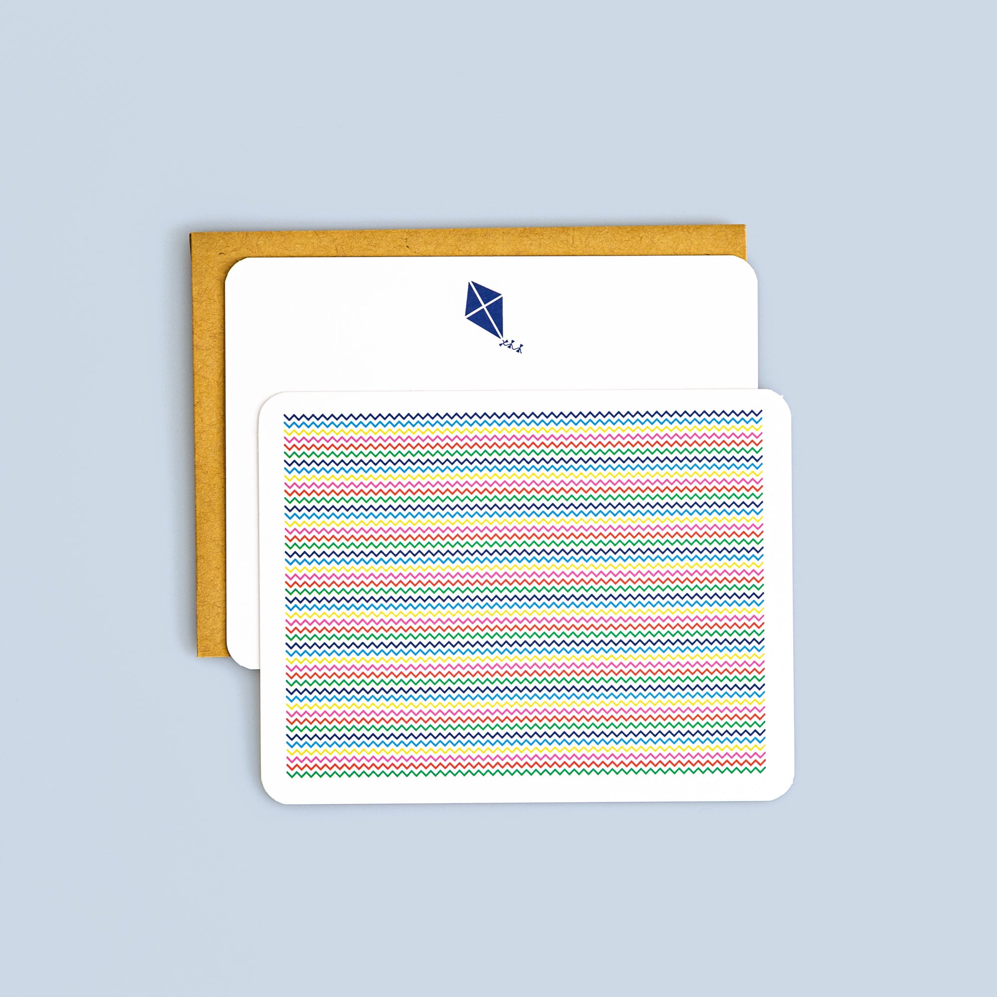 Set of flat cards with colorful zig zag pattern and blue kite illustration, paired with kraft envelope on light blue background