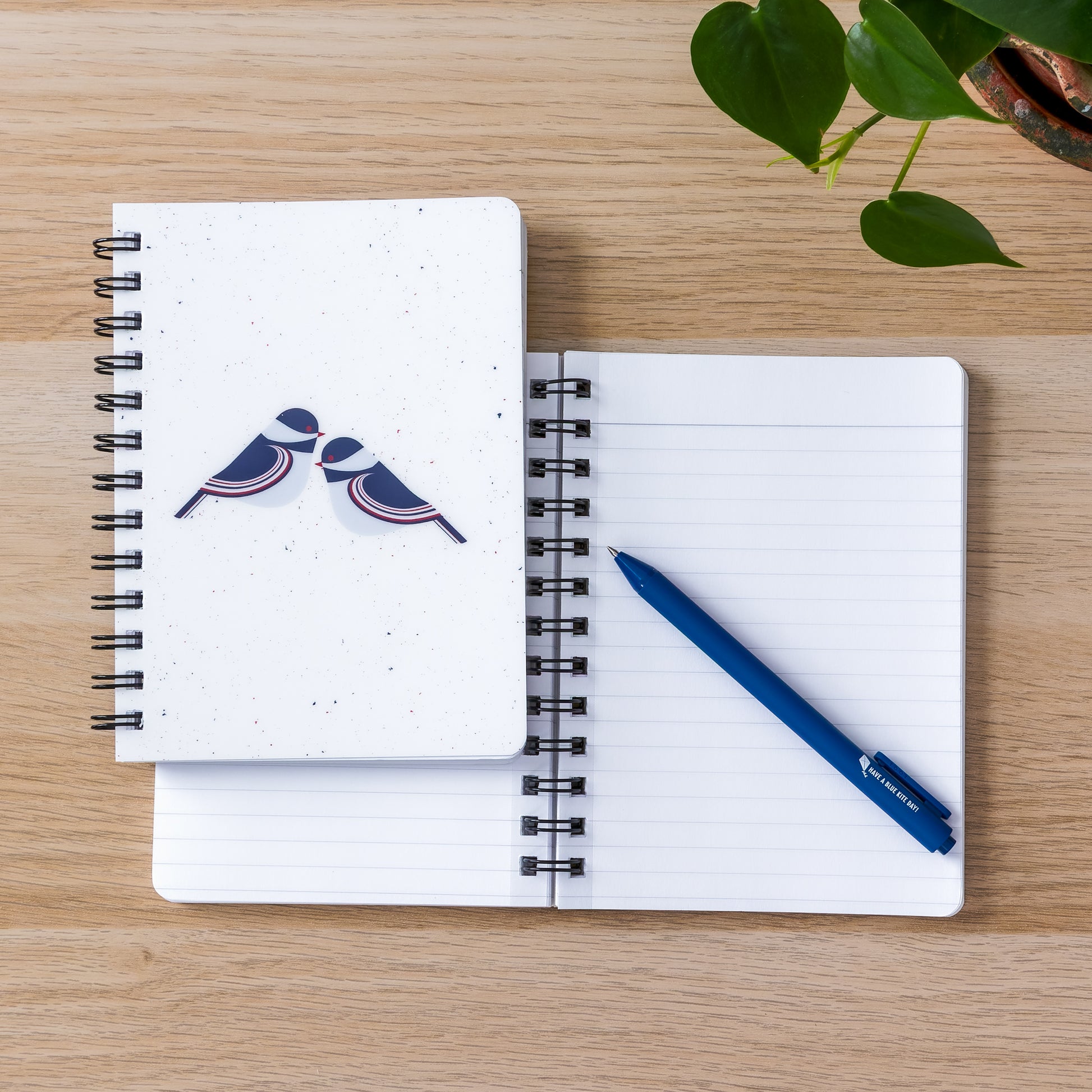 Spiral-bound notebooks with modern chickadee design on wooden surface, blue pen, and green leaves, perfect for jotting down thoughts and ideas