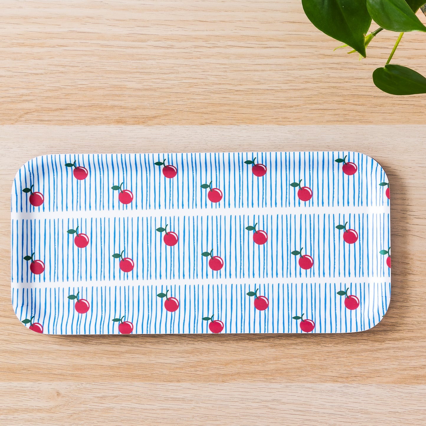 Modern rectangular birch tray with blue striped pattern and red cherry design, placed on wooden surface with green leaves in corner, showcasing stylish and eco-friendly serving option for home decor