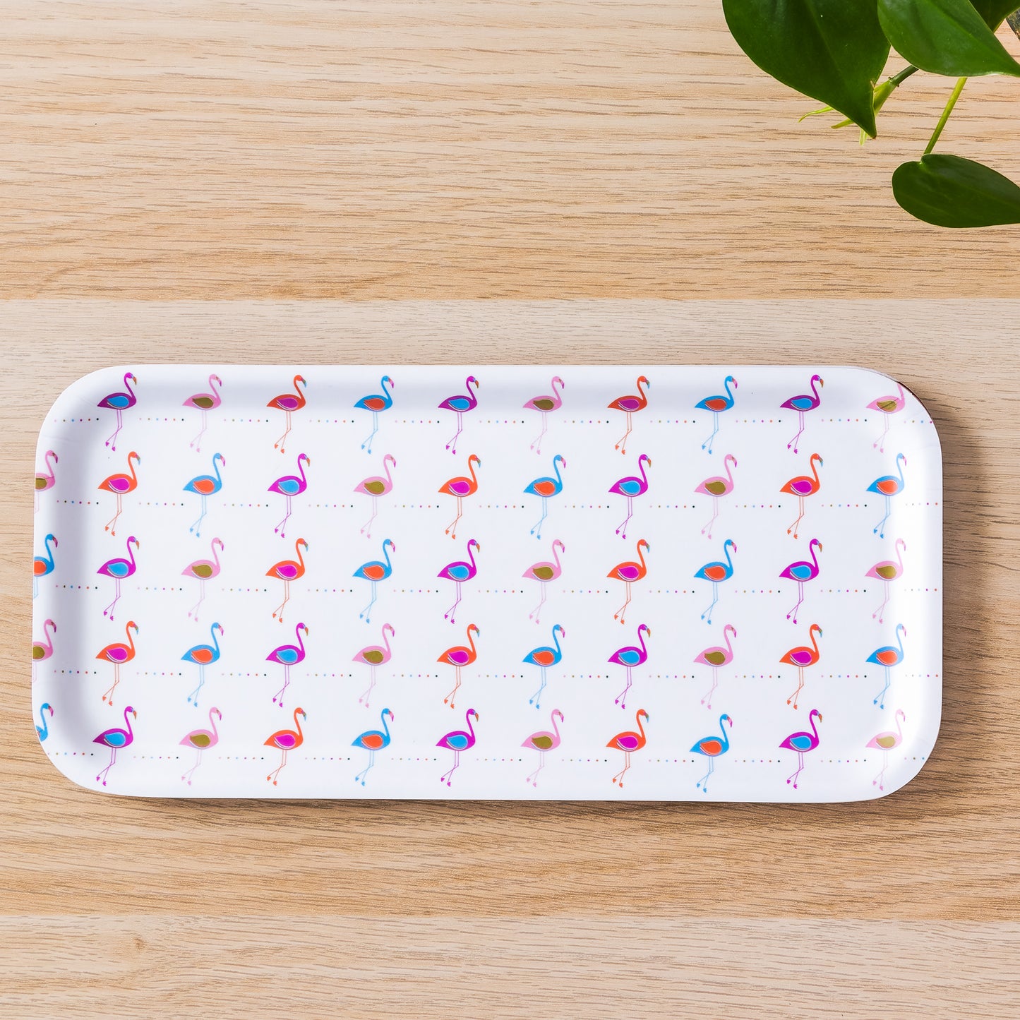 Rectangular birch tray with colorful flamingo pattern in pink and blue, displayed on wooden surface with green plant leaves visible, perfect for modern tropical decor and serving snacks