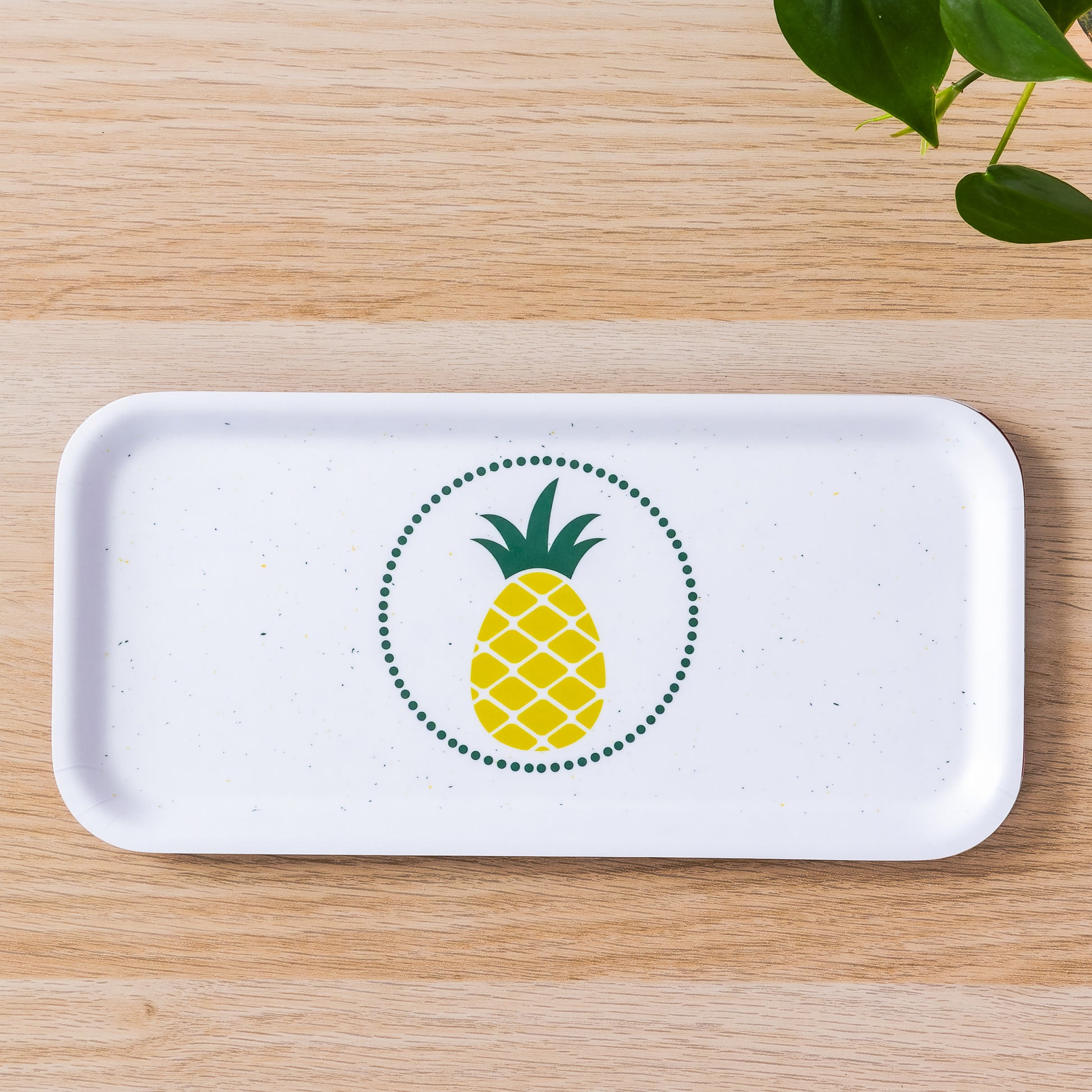 Modern white rectangular birch tray with yellow and green pineapple design centered in green dotted circle, displayed on wooden surface with plant leaves visible